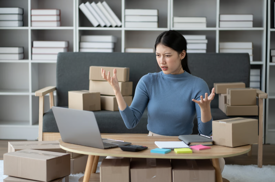 A woman at a table with boxes and a laptop, contemplating the disconnect between social media engagement and sales.