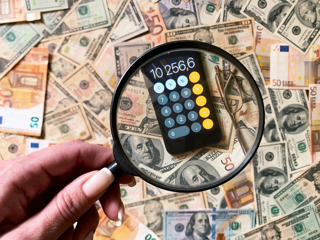 A close-up of a magnifying glass focusing on a calculator displaying a financial figure, surrounded by various currencies, symbolizing the hidden costs of inconsistent creative strategies in branding.