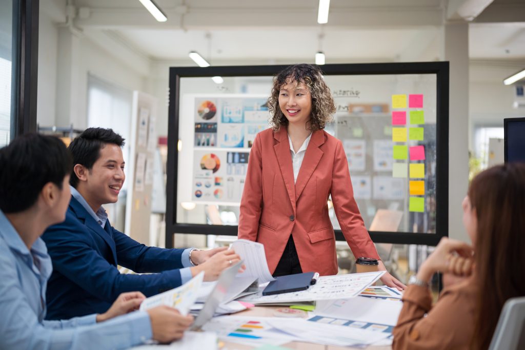 A team of professionals discussing creative concepts around a table, with visual aids in the background, representing structured creative management and collaboration to ensure brand consistency.